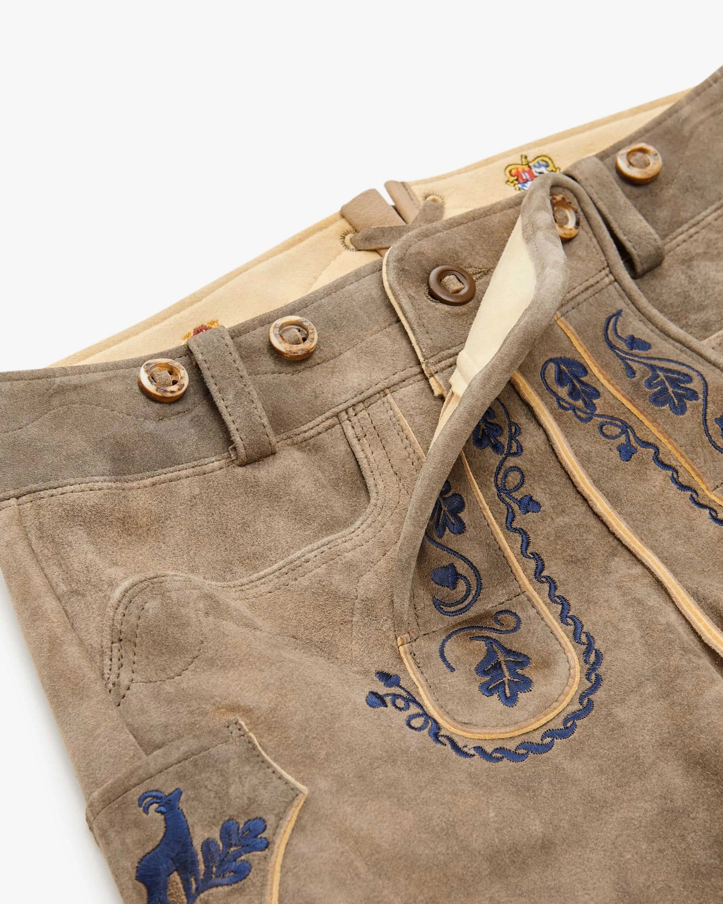 Brown leather pants with blue embroidery on a wooden surface