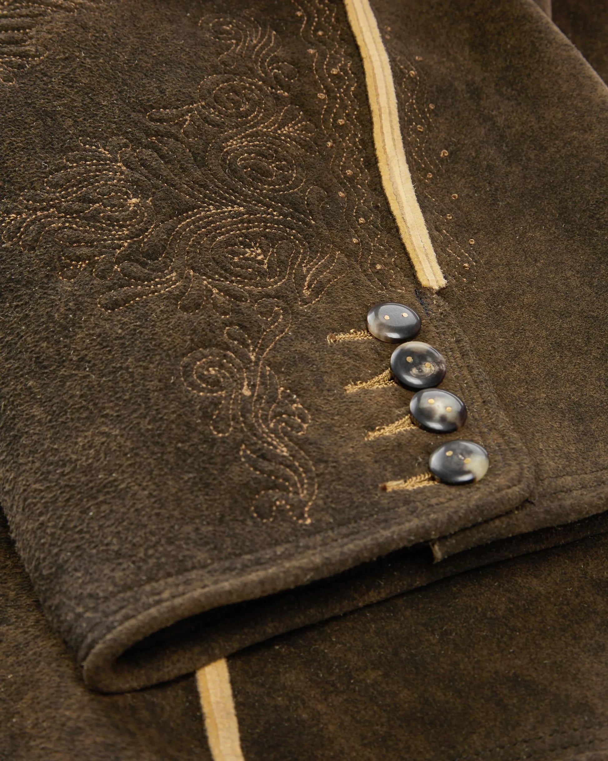 Close-up of a brown textured fabric with embroidered patterns and buttons.