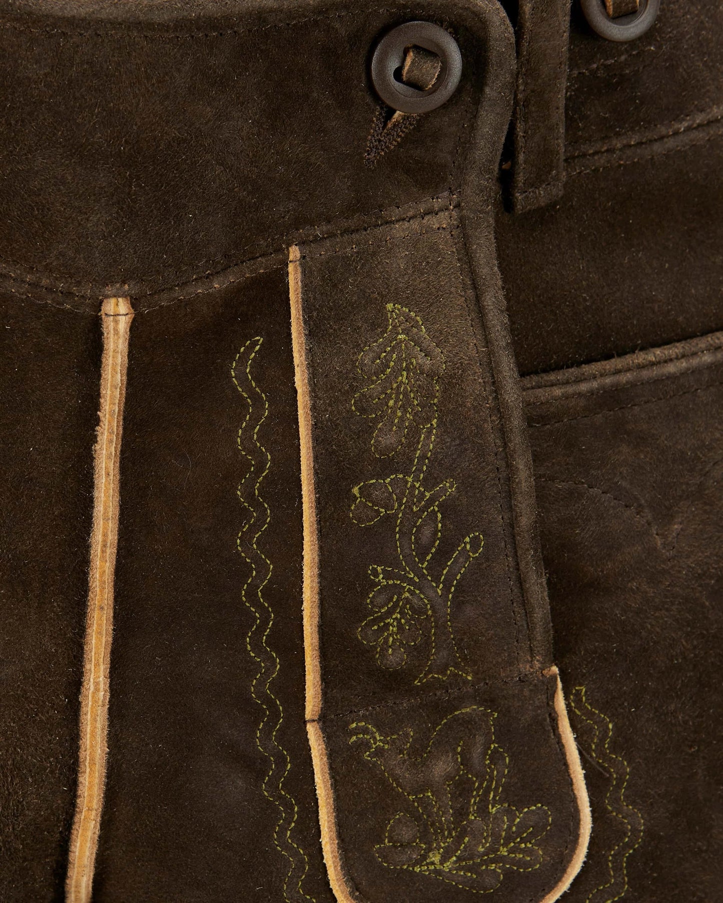 Close-up of brown suede fabric with embroidered designs and buttons.