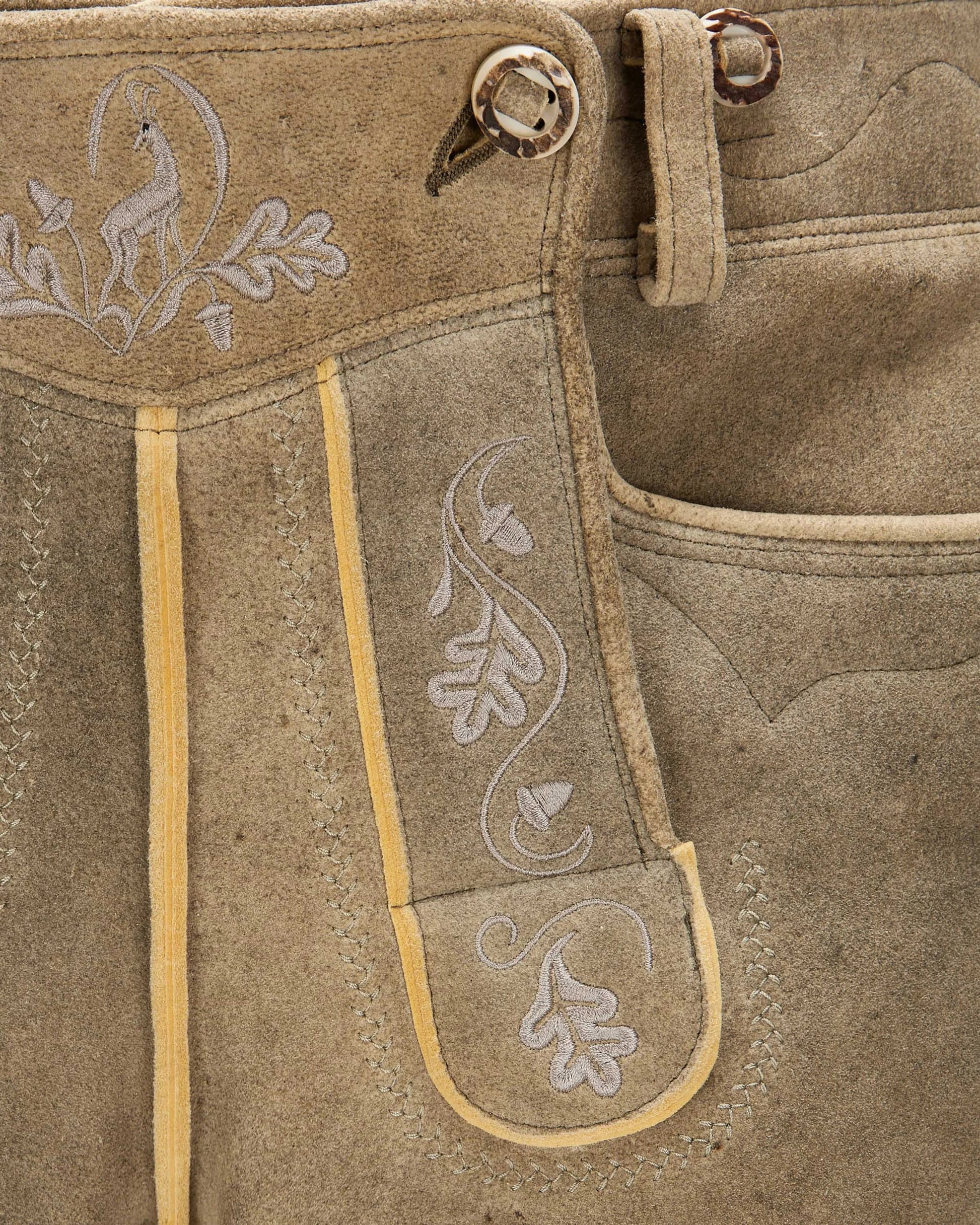 Close-up of brown leather pants with embroidery and button details