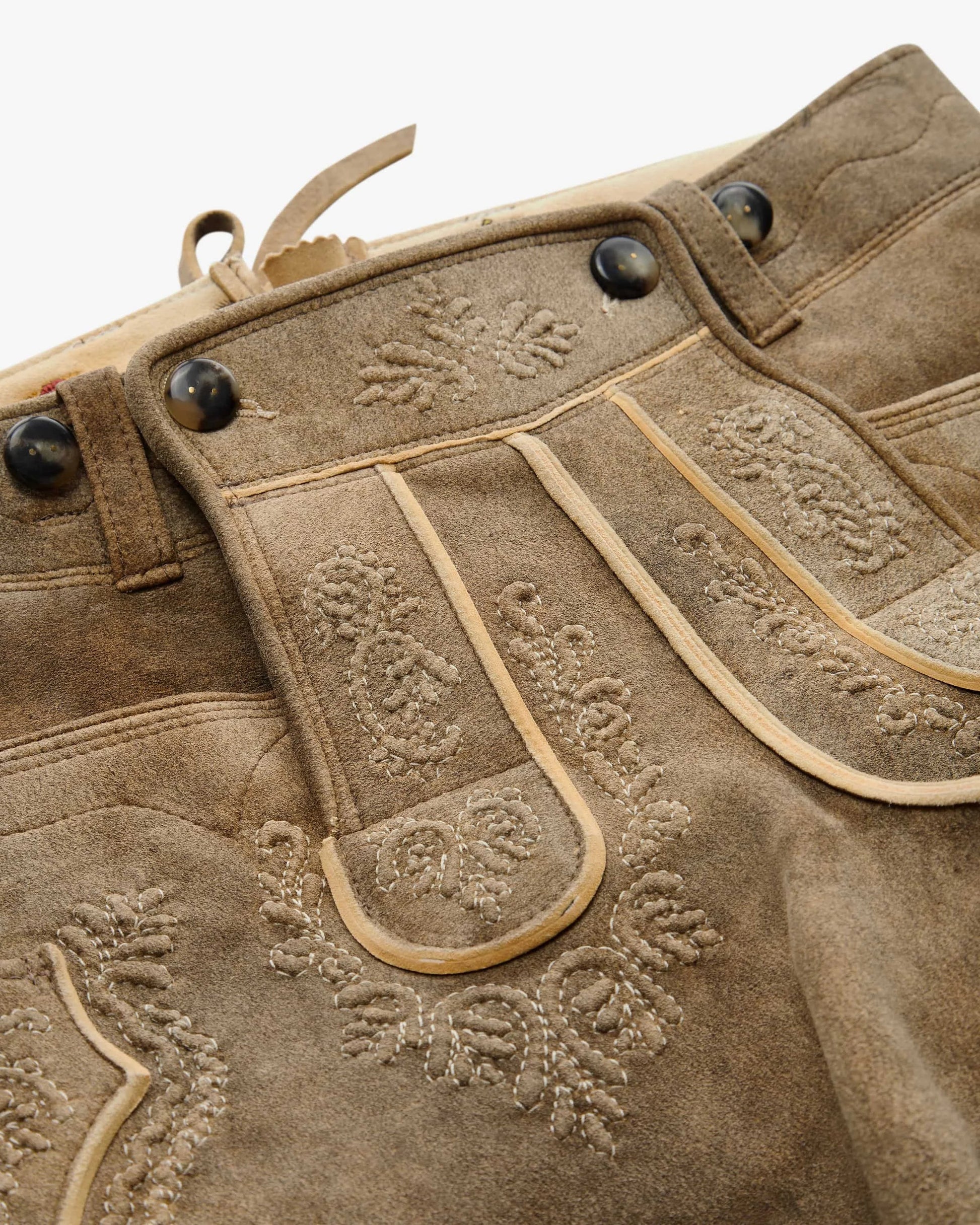 Close-up of brown leather pants with intricate stitching and decorative elements.