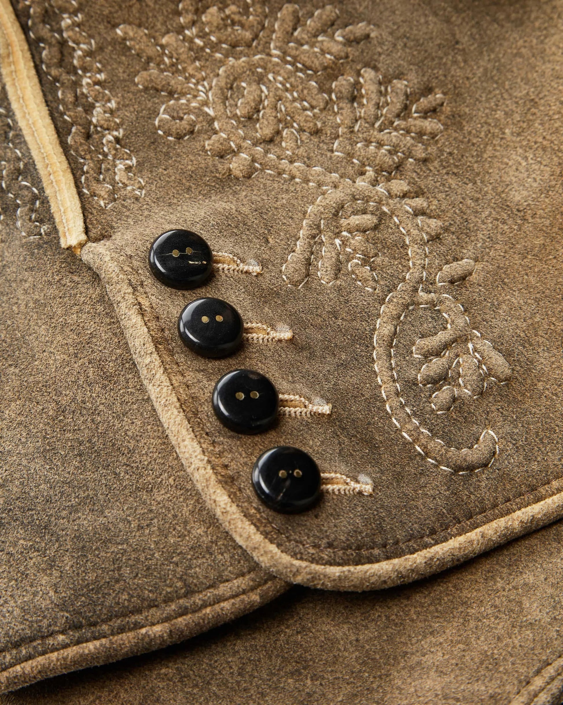 Close-up of a brown fabric with embroidered design and black buttons.