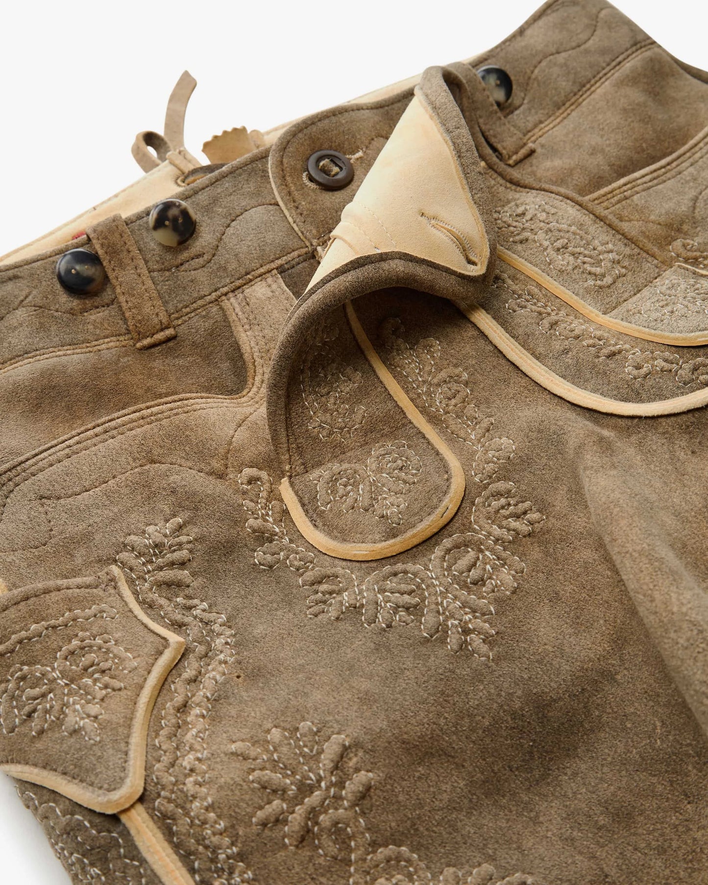 Close-up of a brown leather jacket with floral embroidery on a white background