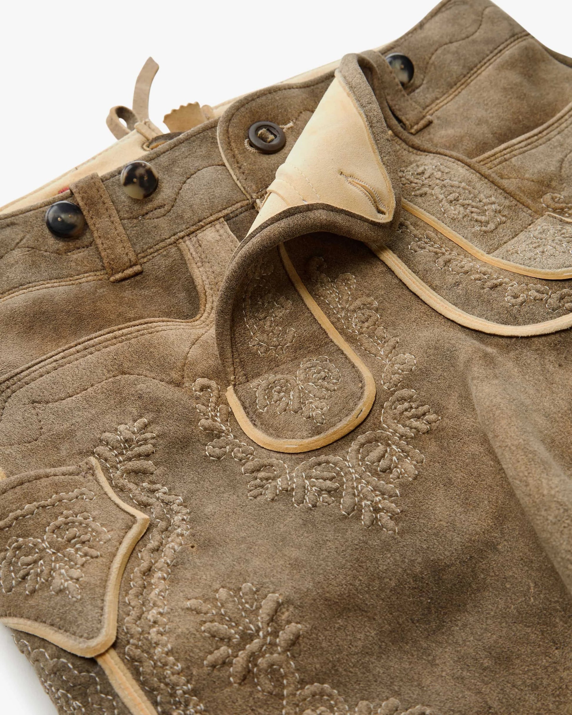 Close-up of a brown leather jacket with floral embroidery on a white background