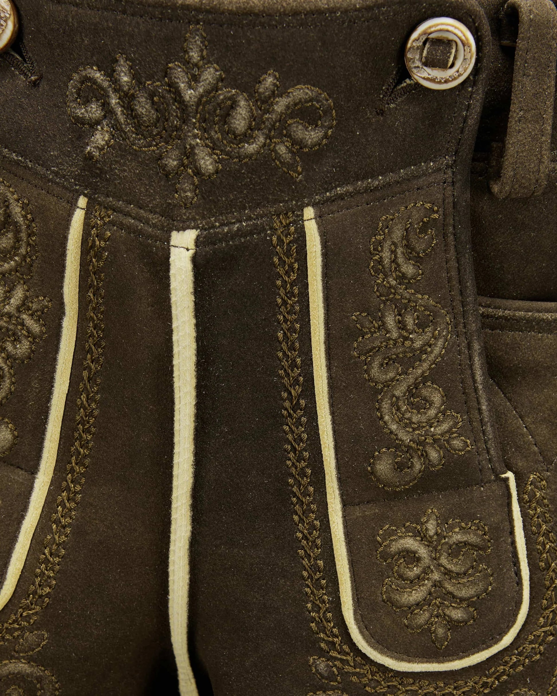 Close-up of brown leather pants with decorative stitching and buttons.