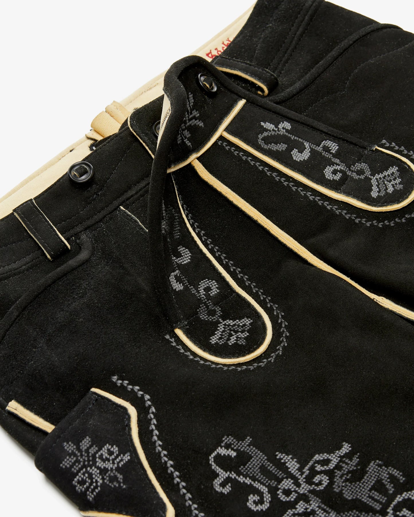 Close-up of black pants with decorative white stitching on a white background