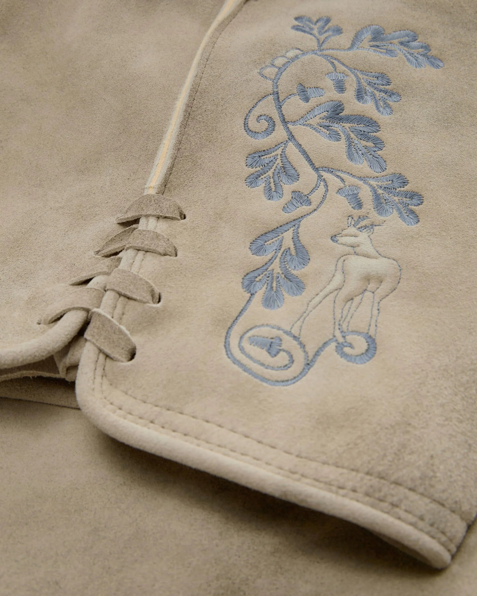 Close-up of beige fabric with blue embroidered design on a garment.