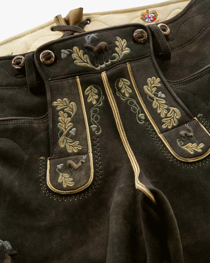 Close-up of dark brown leather pants with gold embroidery on a white background