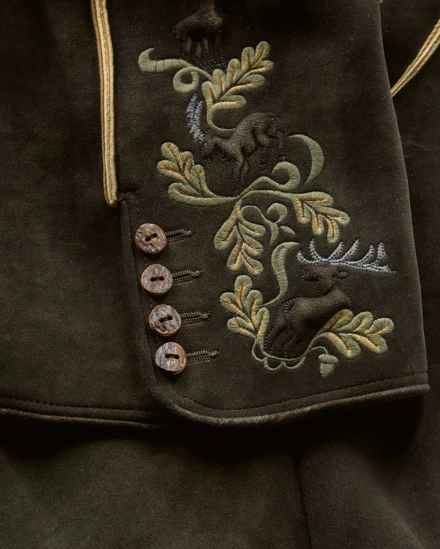 Embroidered design on a dark fabric with deer and foliage patterns.