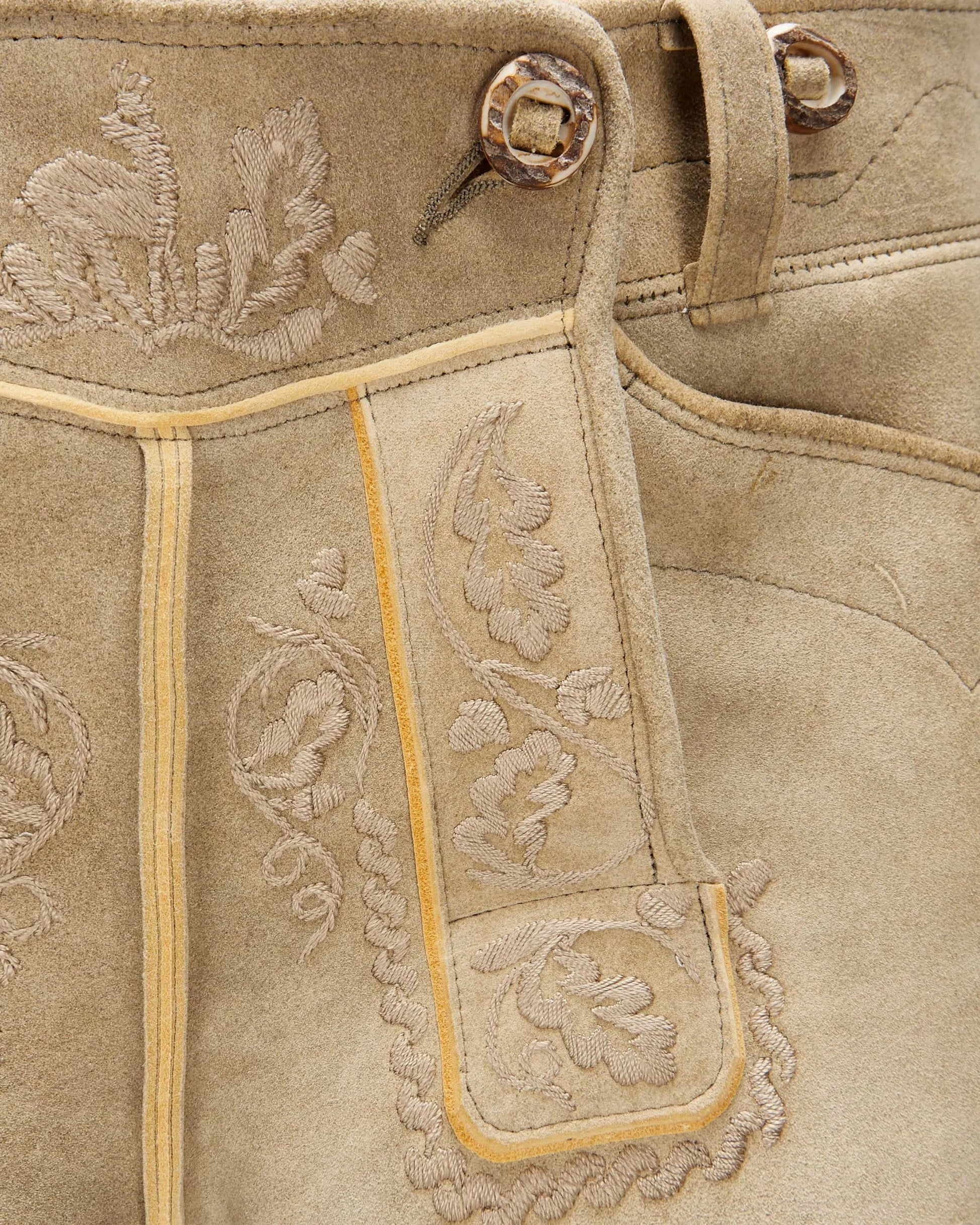 Close-up of beige leather boot with floral embroidery and metal eyelets.