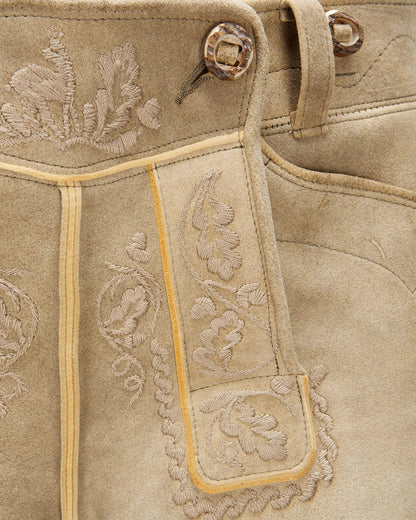 Close-up of beige leather boot with floral embroidery and metal eyelets.