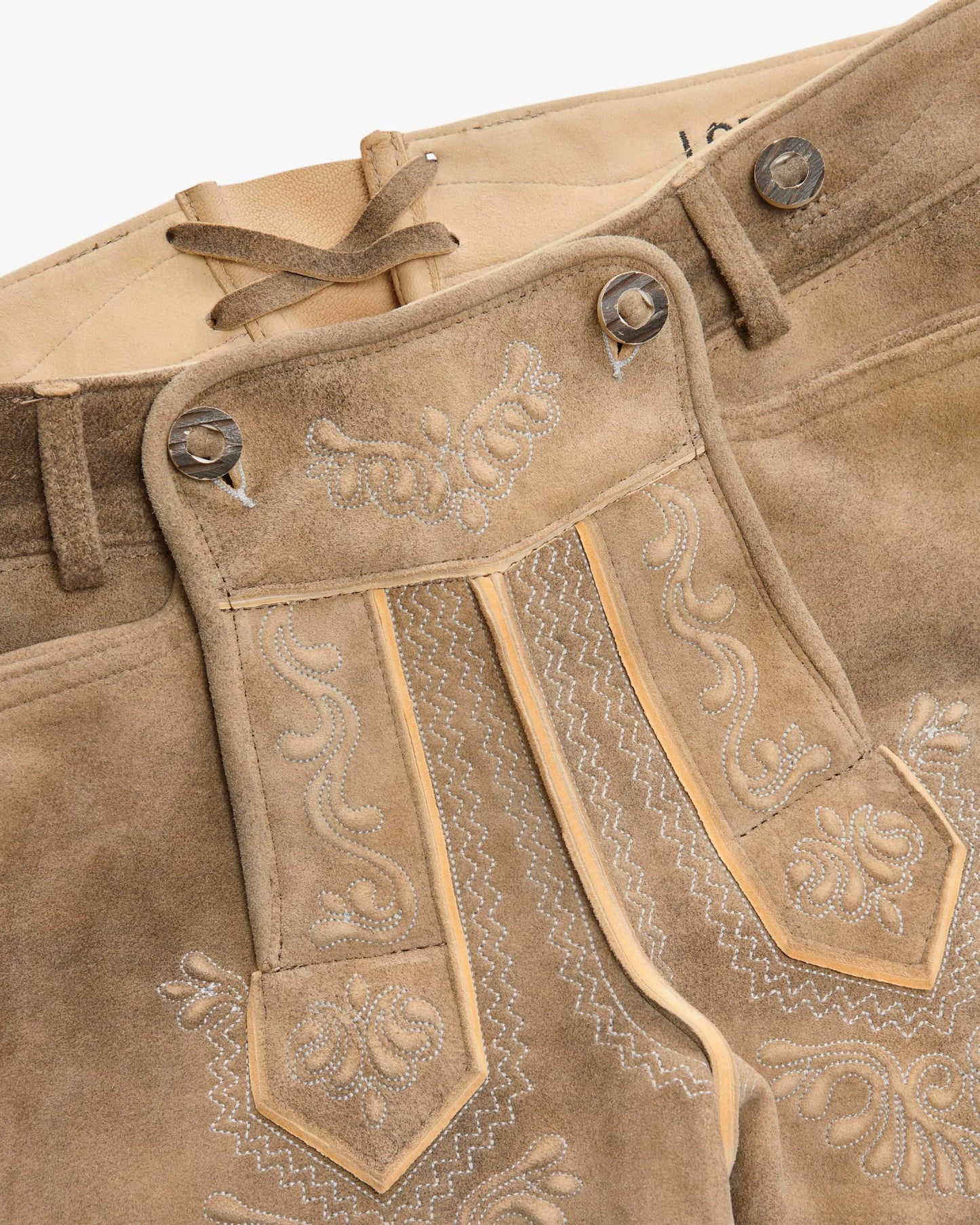 Close-up of brown leather pants with intricate embroidery and stitching details.