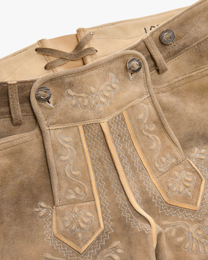 Close-up of brown leather pants with intricate embroidery and stitching details.