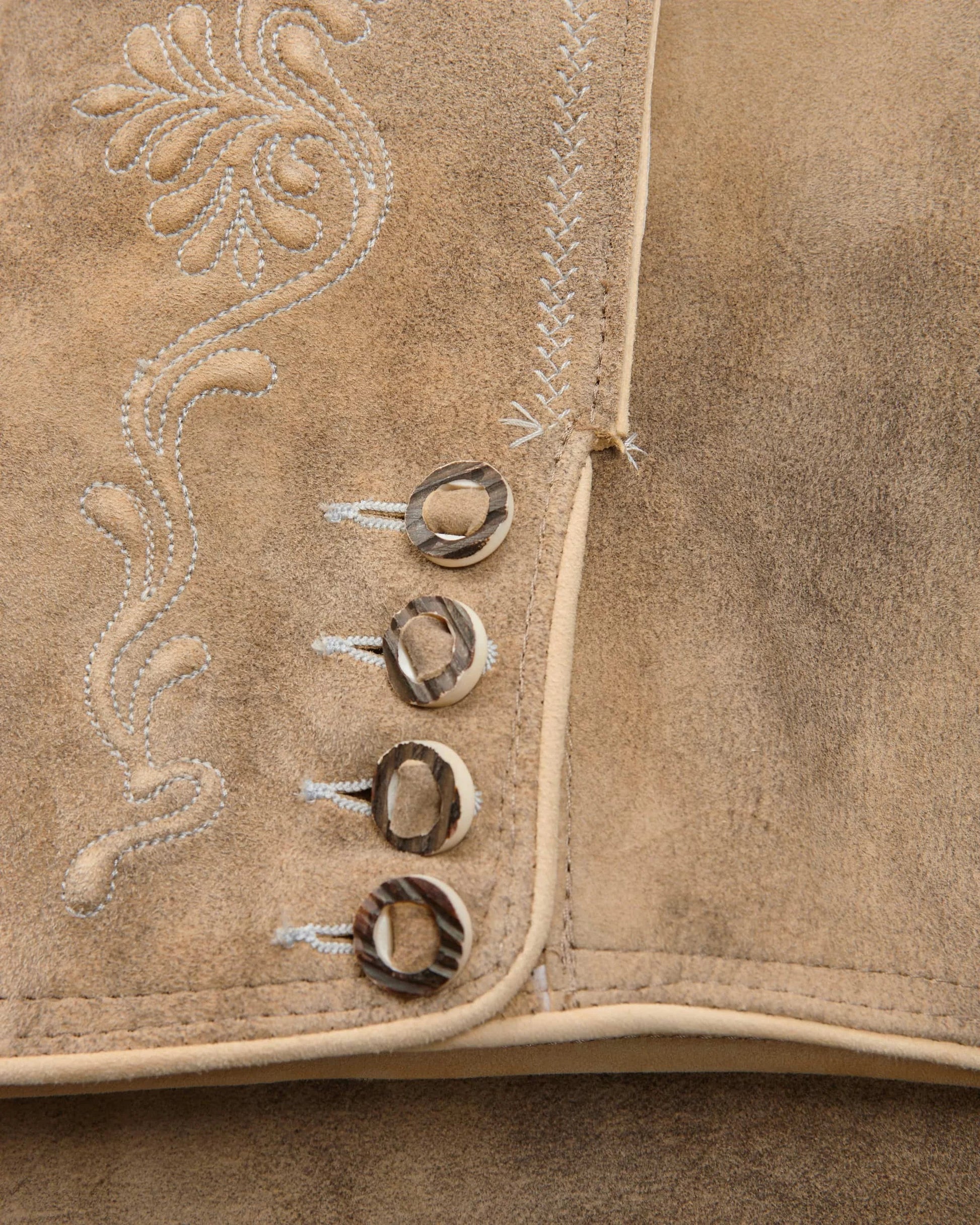 Close-up of a brown leather vest with decorative stitching and buttons.