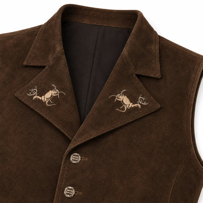 Close-up of a brown suede vest with notched lapels featuring embroidered deer motifs on each side, a dark brown inner lining, and decorative buttons on the front.