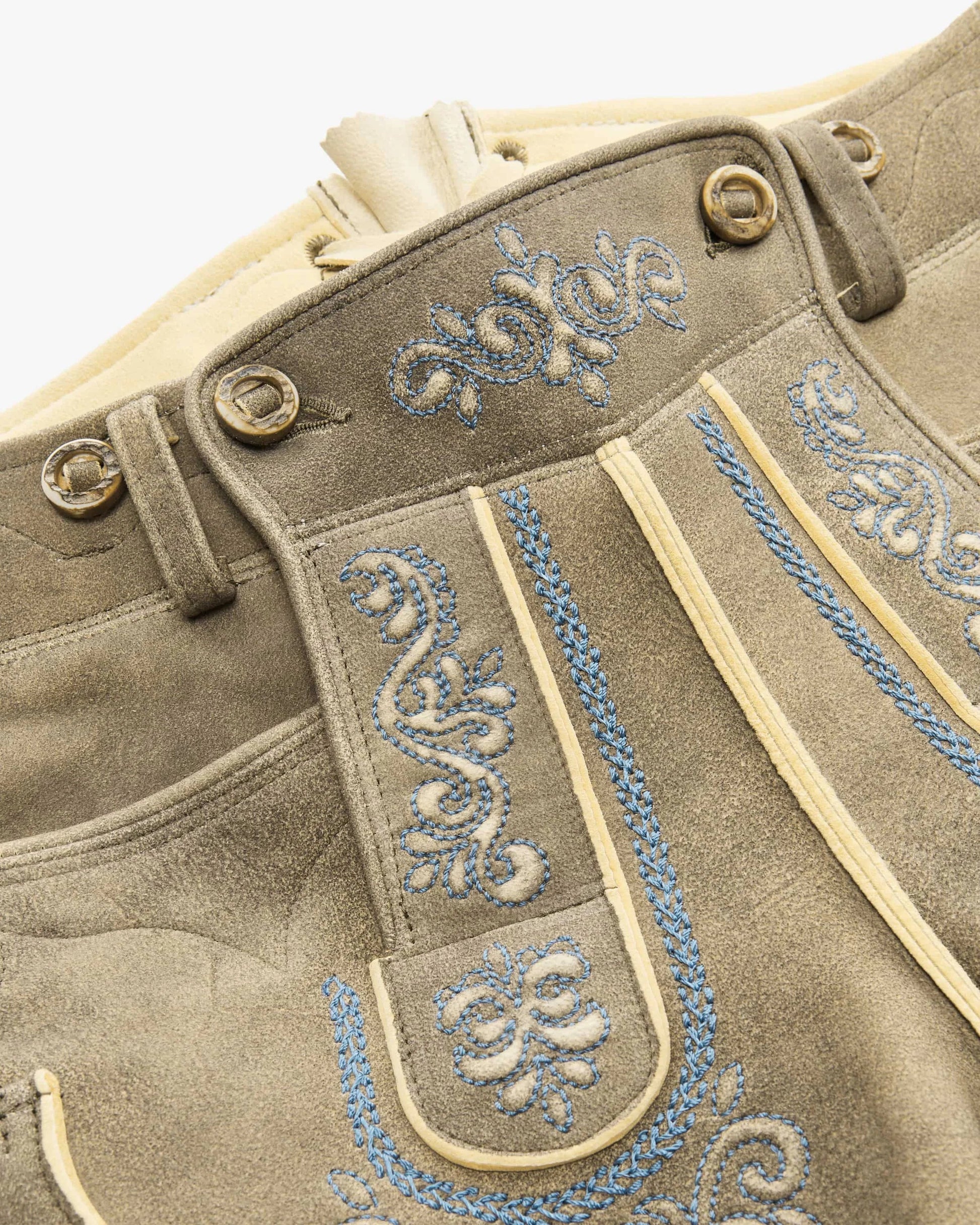 Close-up of a brown leather outfit with blue embroidery on a white background