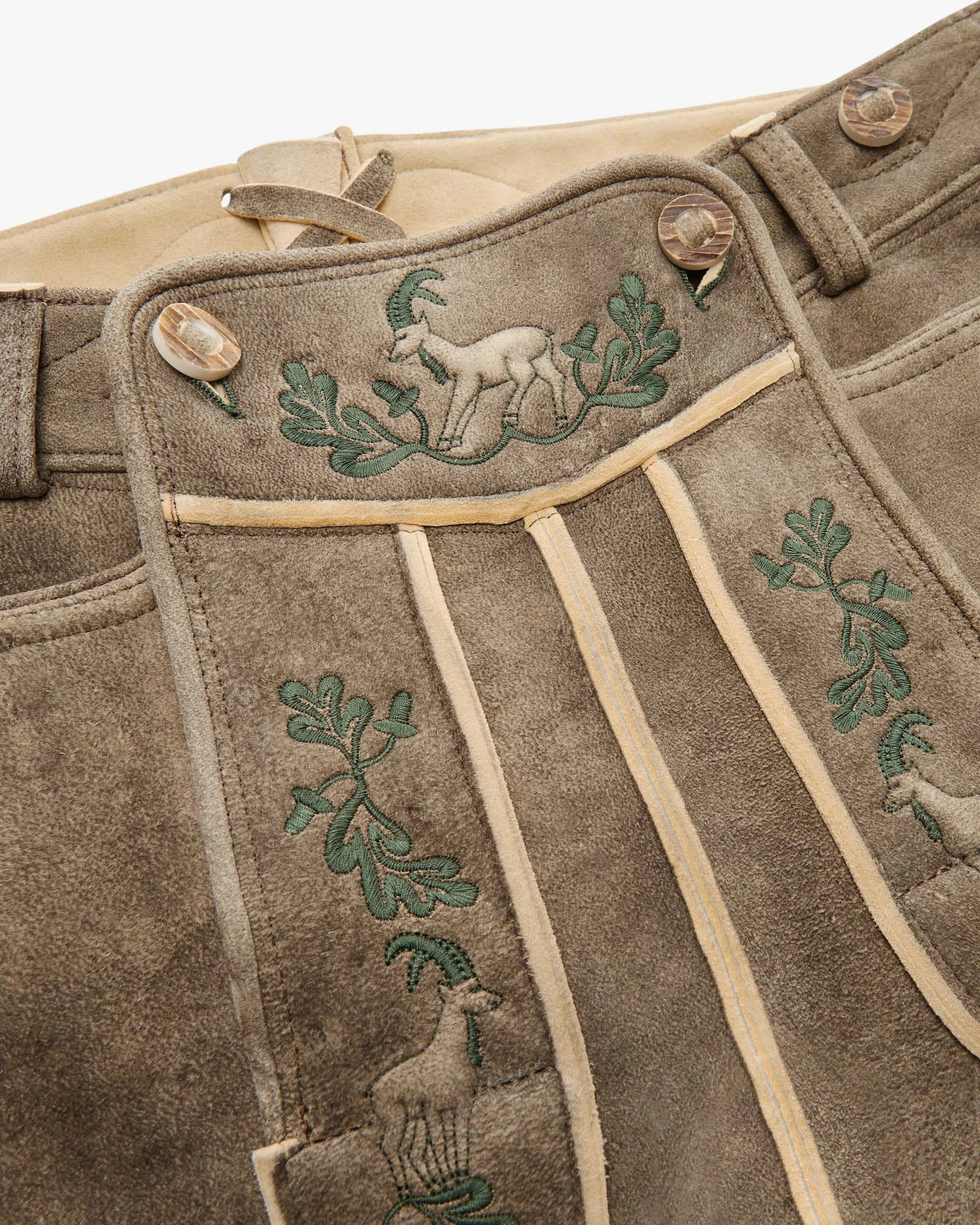 Brown leather pants with embroidered green designs of deer and leaves on a beige background