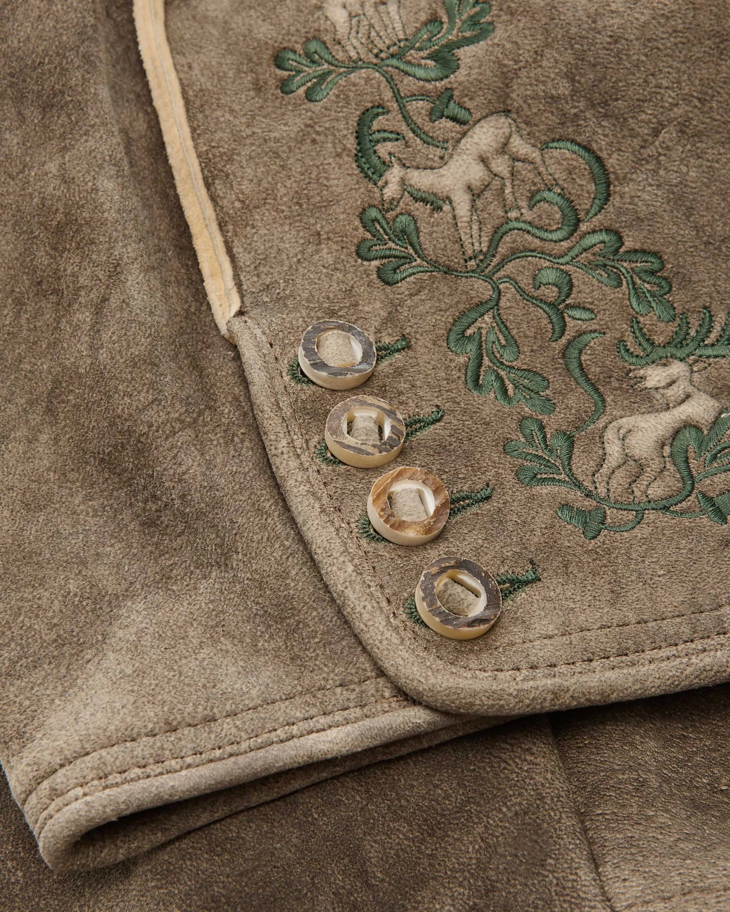 Close-up of a brown fabric with embroidered deer and foliage design.