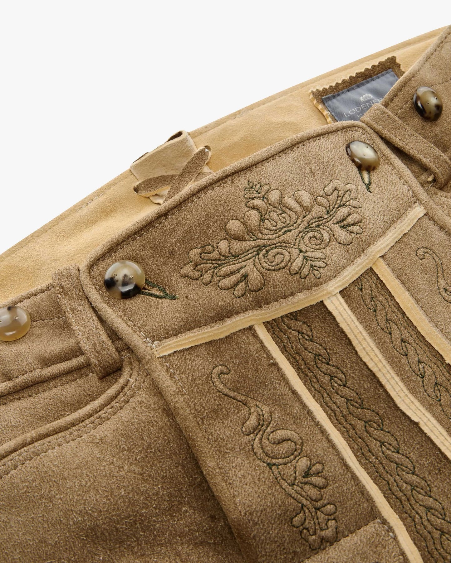 Close-up of a beige fabric with intricate embroidery and buttons on a white background