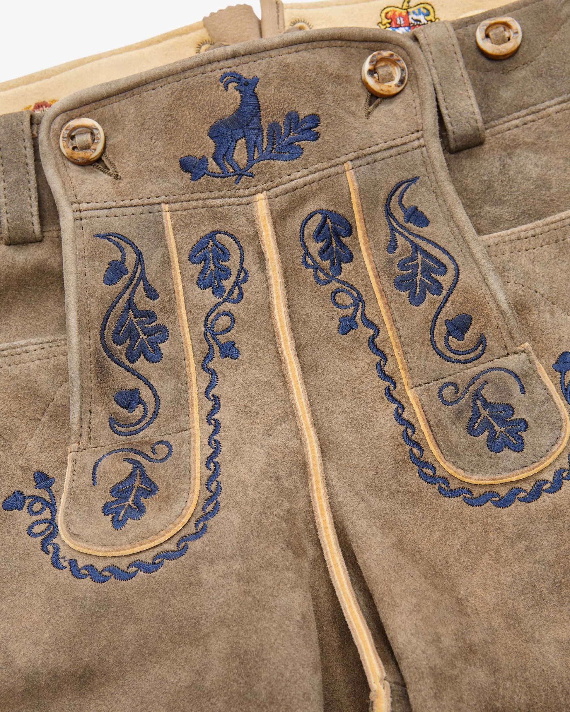 Brown leather pants with blue embroidery and gold buttons on a white background