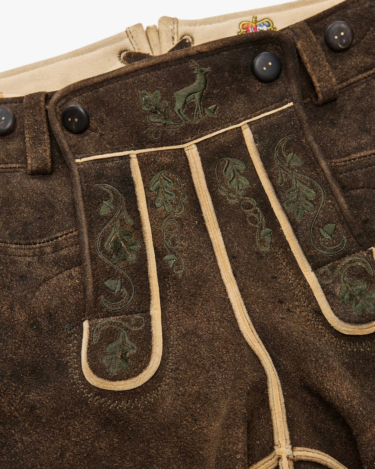 Brown leather pants with green embroidery and buttons, featuring a visible brand logo.