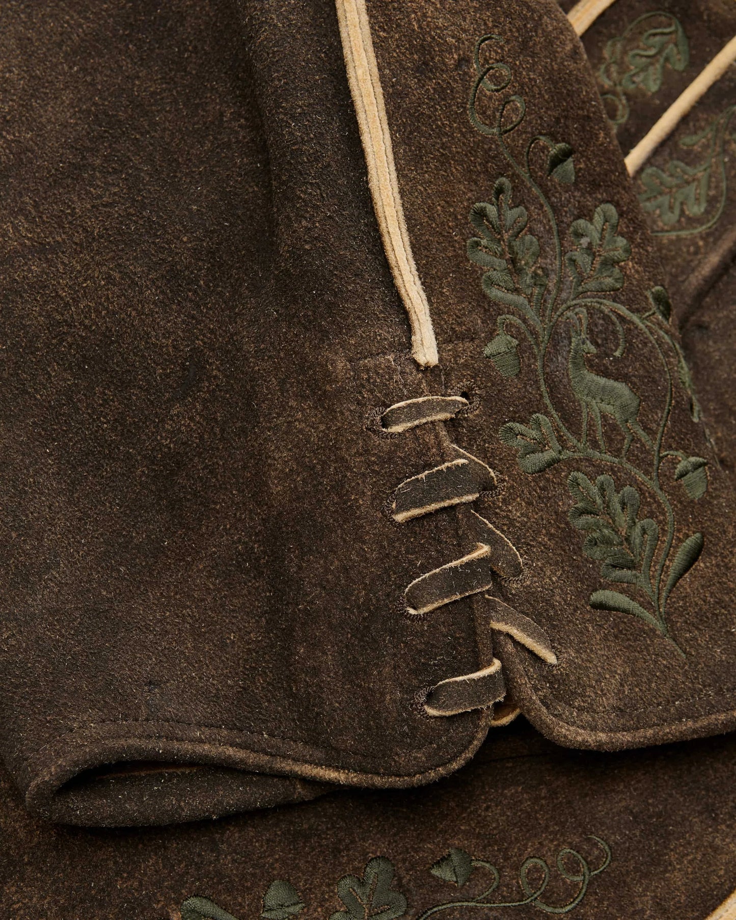 Close-up of a brown fabric with embroidered green leaves on a garment.