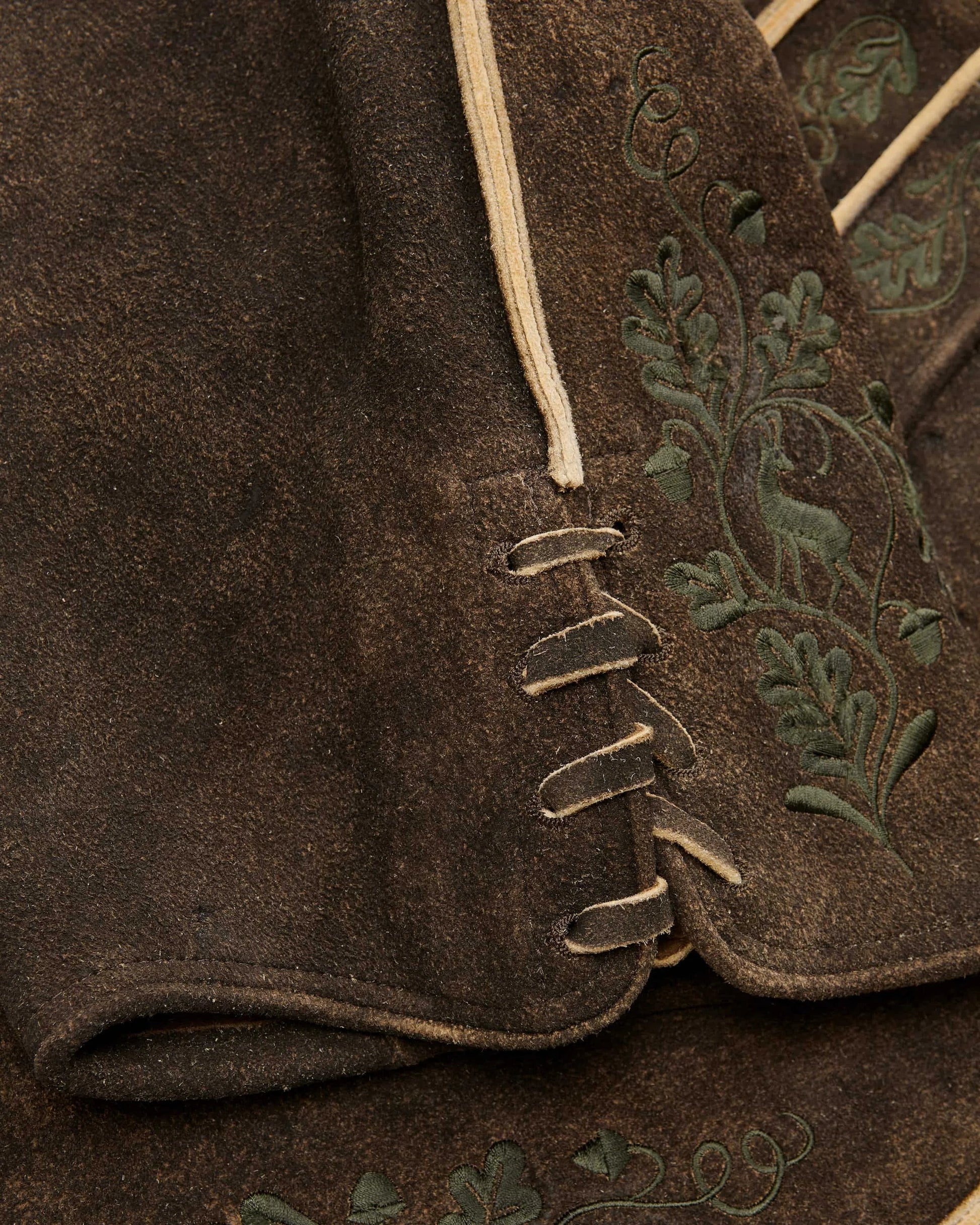 Close-up of a brown fabric with embroidered green leaves on a garment.