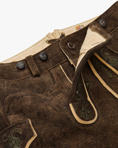 Close-up of brown leather pants with decorative stitching and buttons on a white background