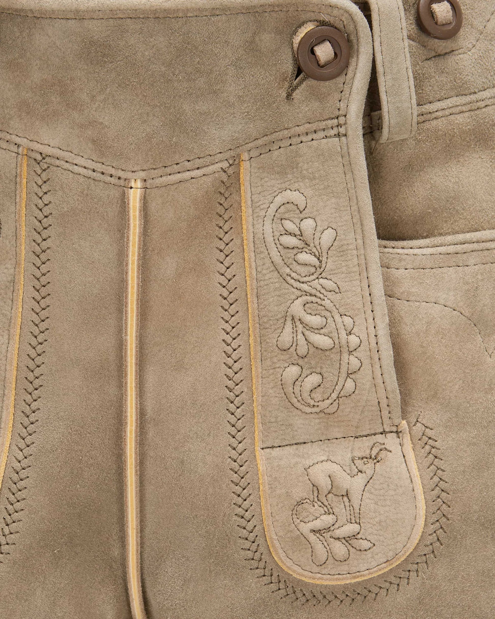Close-up of brown leather pants with intricate stitching and a embroidered design.