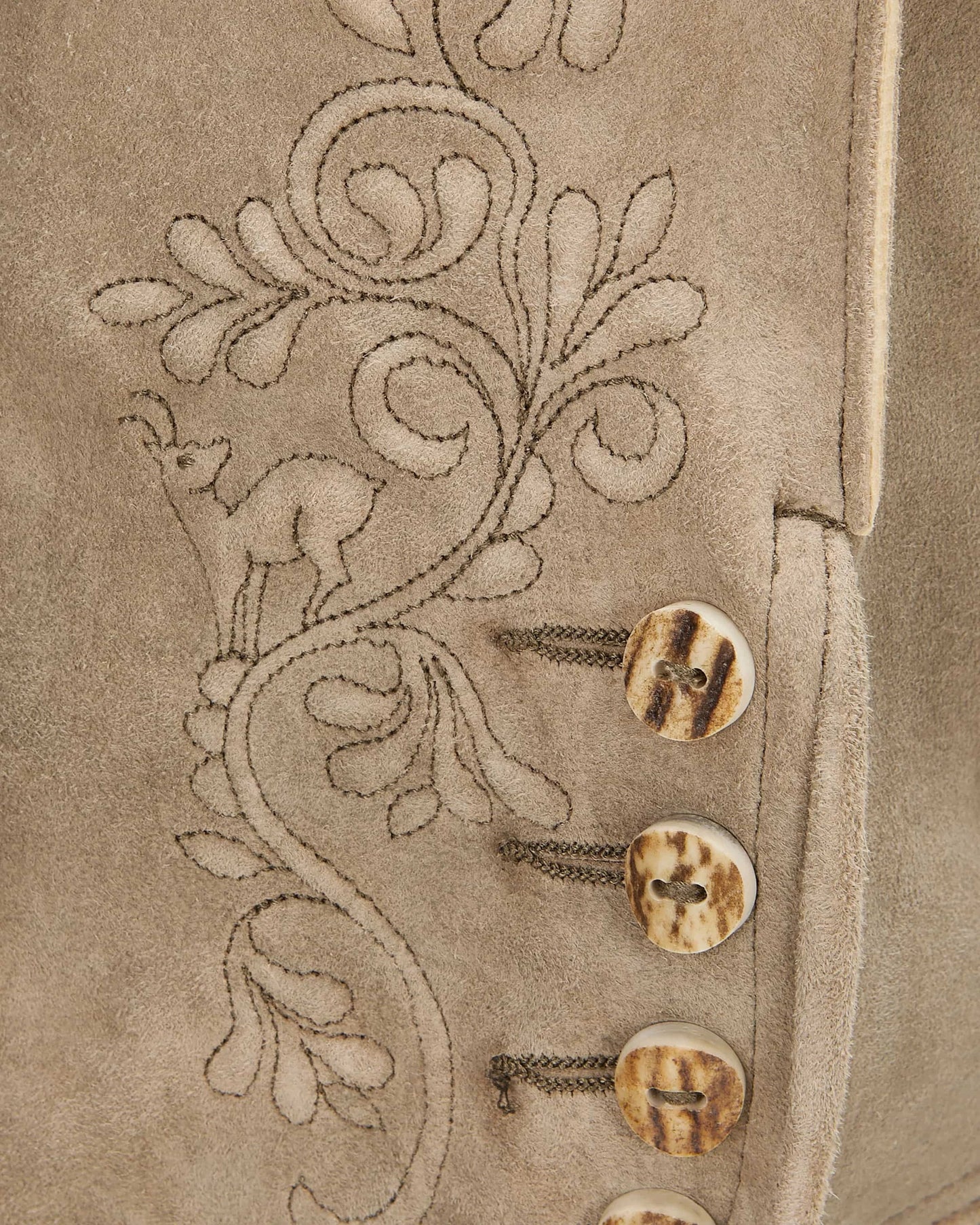 Close-up of a beige fabric with floral embroidery and buttons.