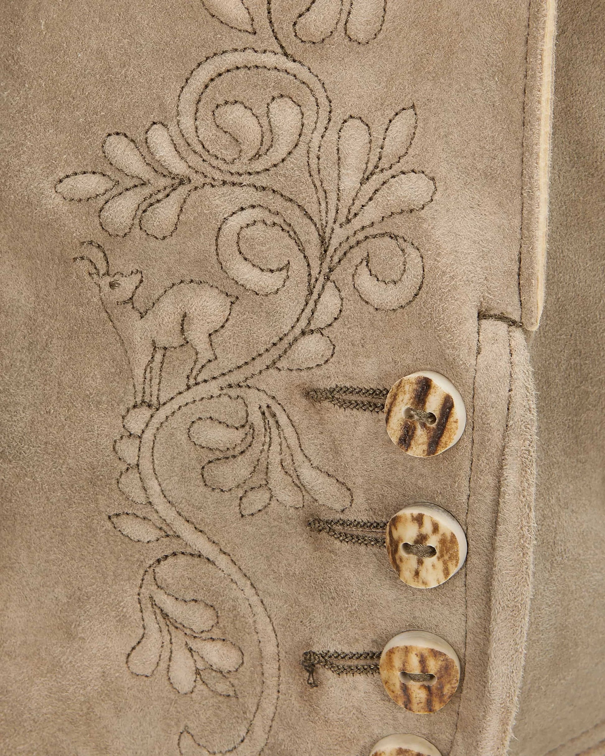 Close-up of a beige fabric with floral embroidery and buttons.