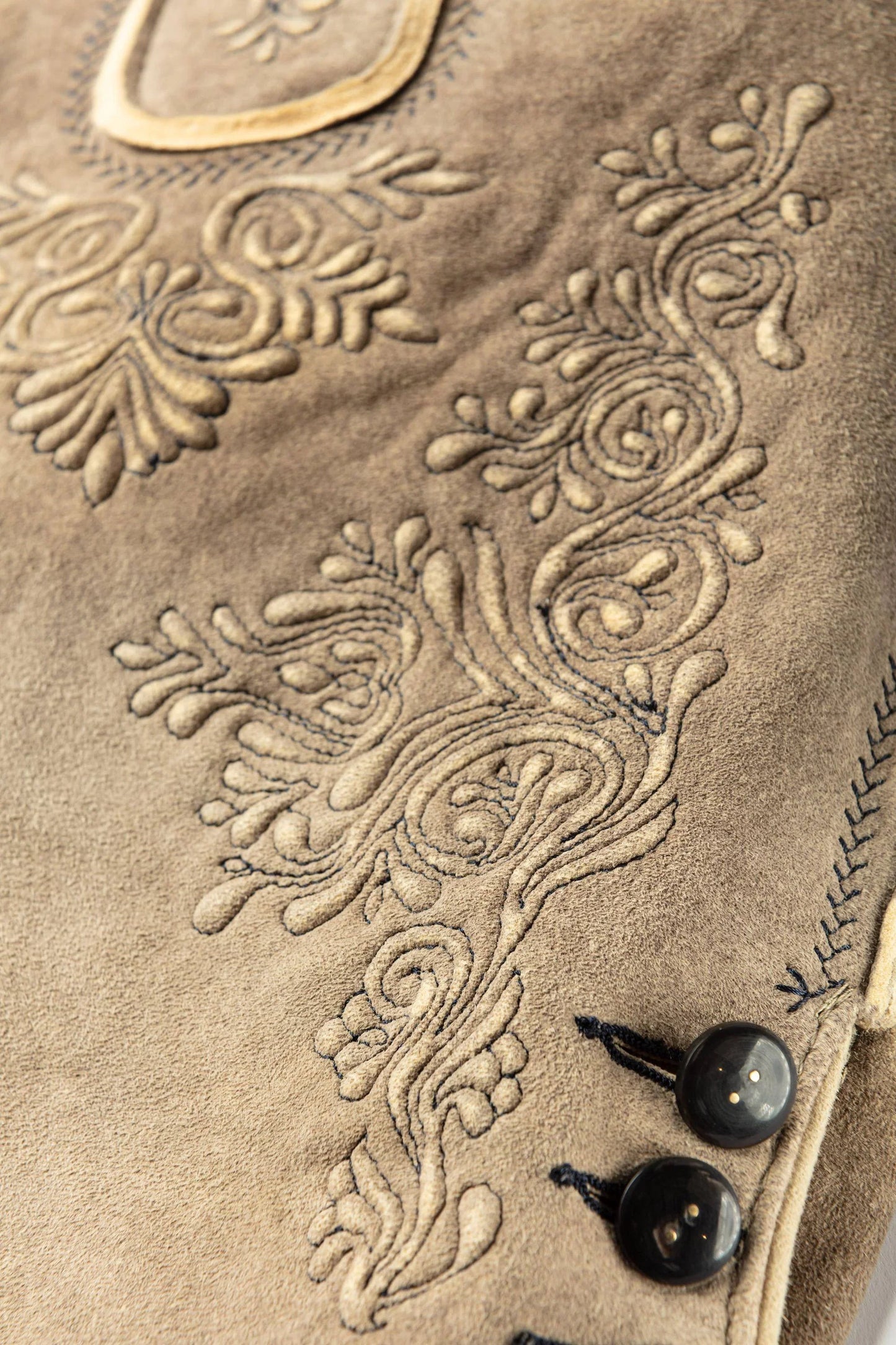 Close-up of a beige fabric with intricate floral embroidery and black buttons.