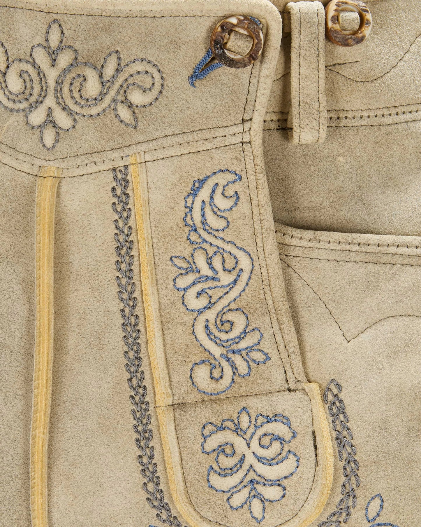 Close-up of beige fabric with intricate blue embroidery and decorative stitching.