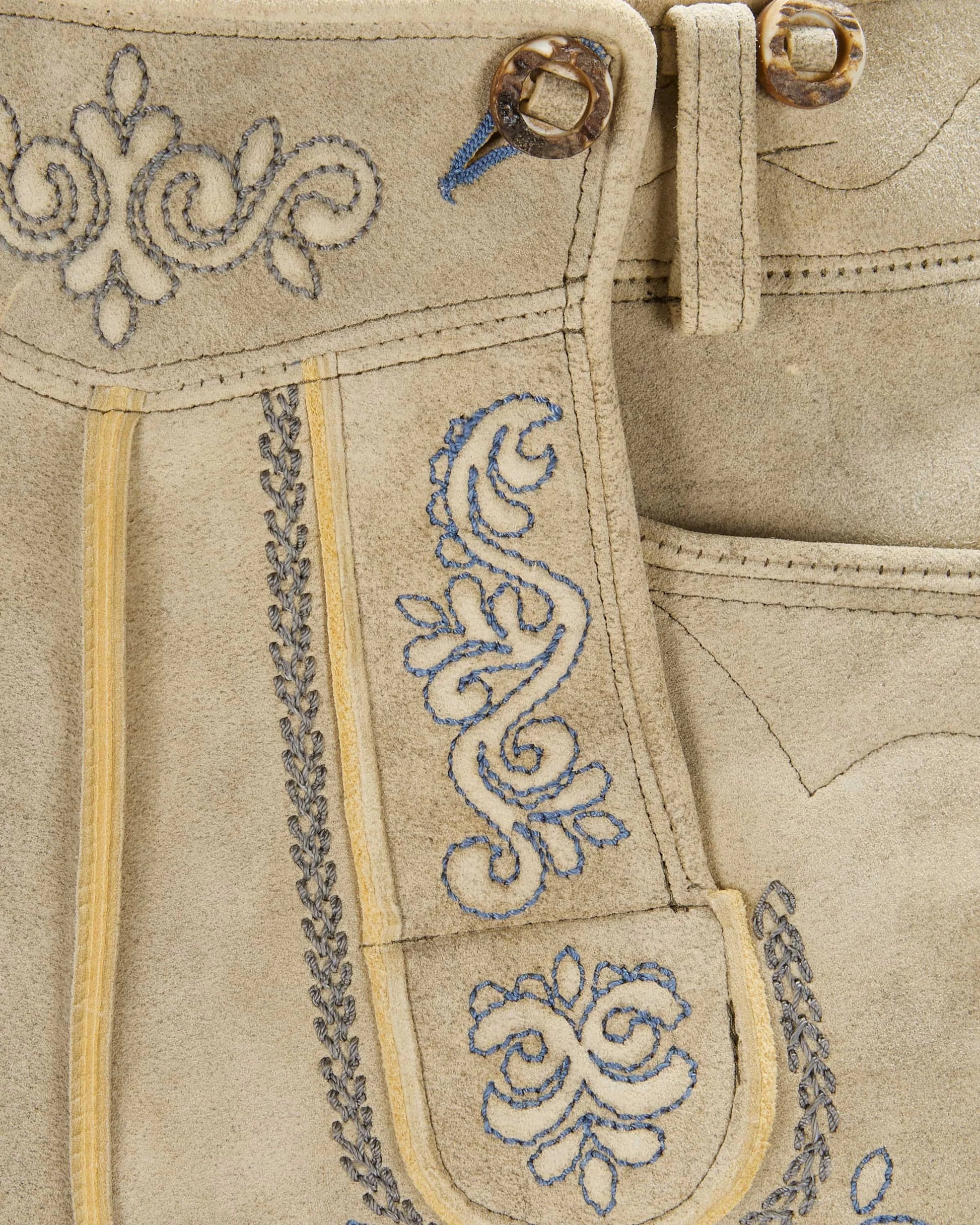 Close-up of beige fabric with intricate blue embroidery and decorative stitching.