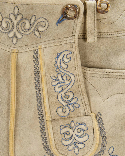 Close-up of beige fabric with intricate blue embroidery and decorative stitching.