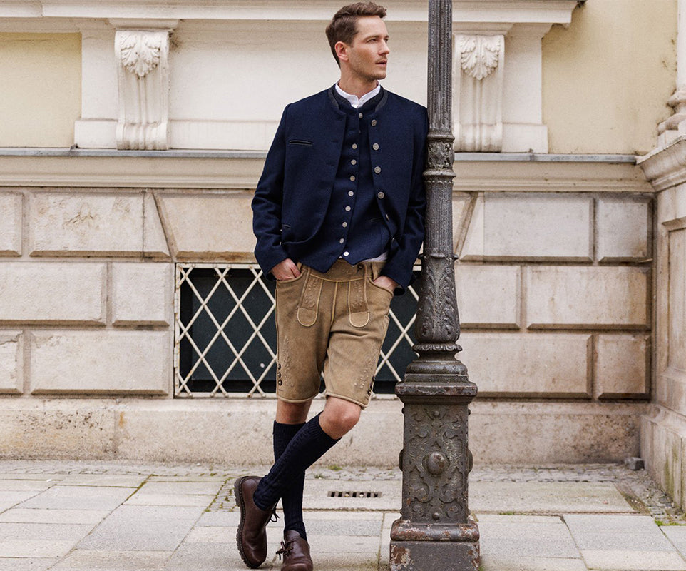 Man in formal attire with a jacket and shorts leaning against a building.