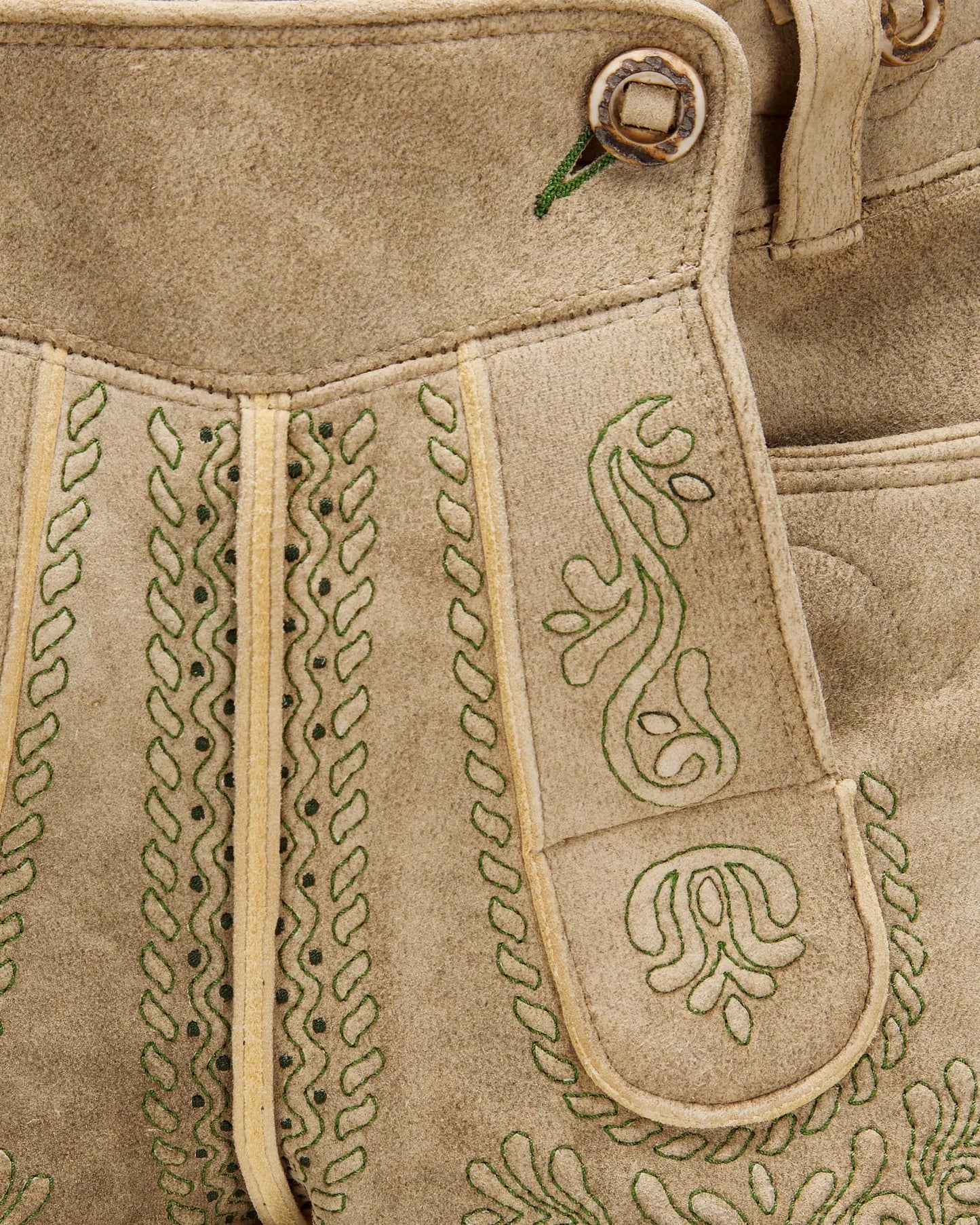 Close-up of a beige leather bag with intricate green embroidery