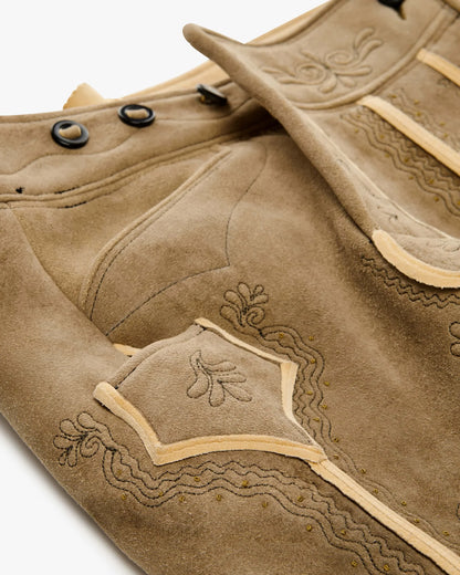 Close-up of a brown leather boot with intricate stitching and decorative elements on a white background