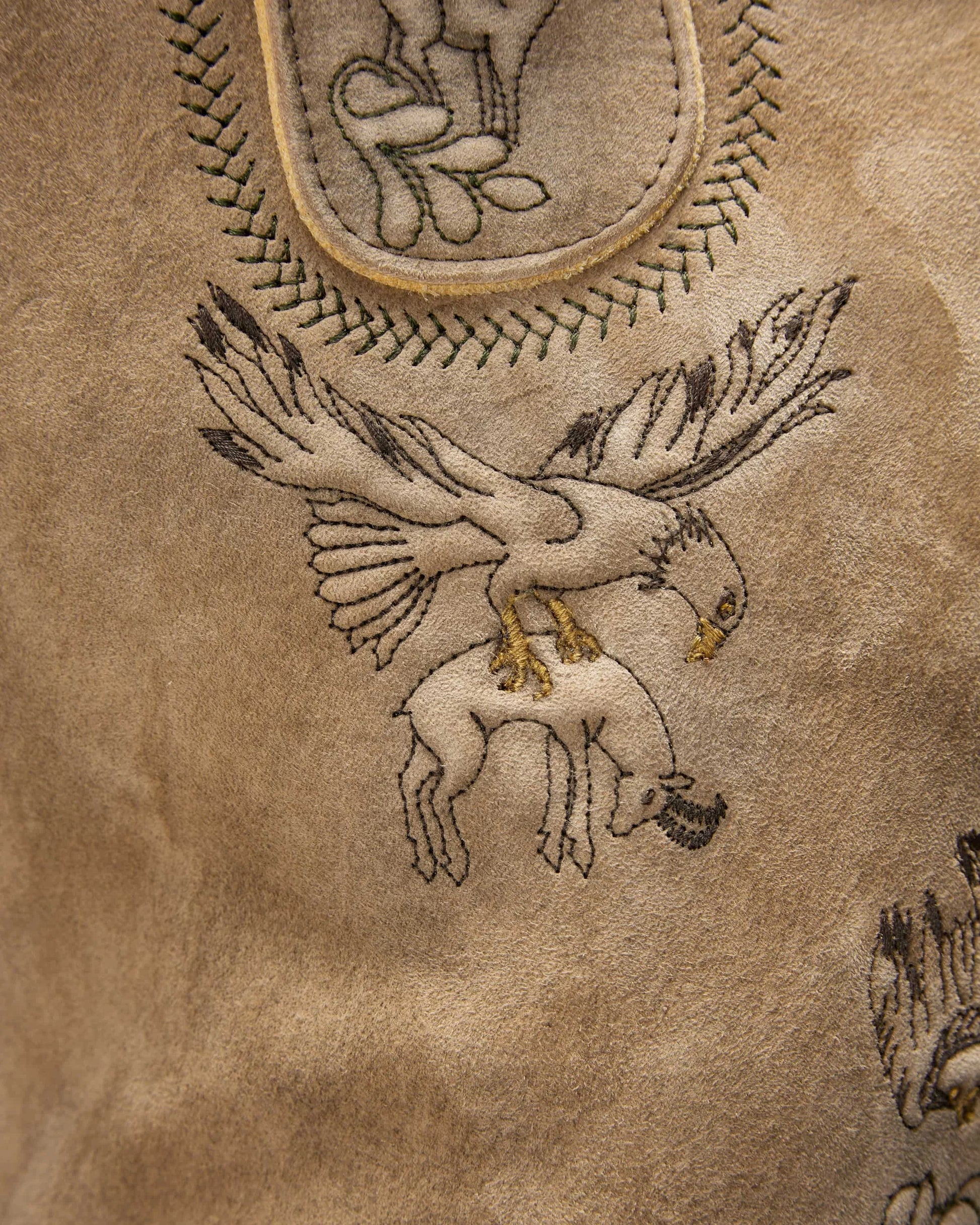 Embroidered design of a bird on a textured brown leather surface