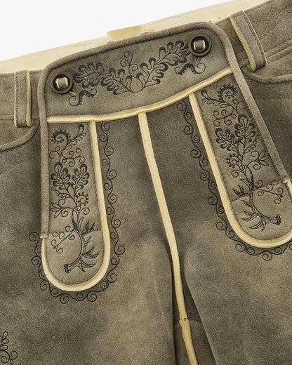 Close-up of brown leather pants with intricate floral embroidery on a beige background