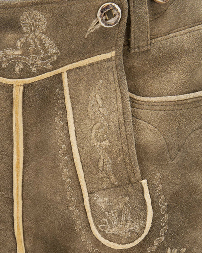 Close-up of brown leather pants with intricate white embroidery on a matching background