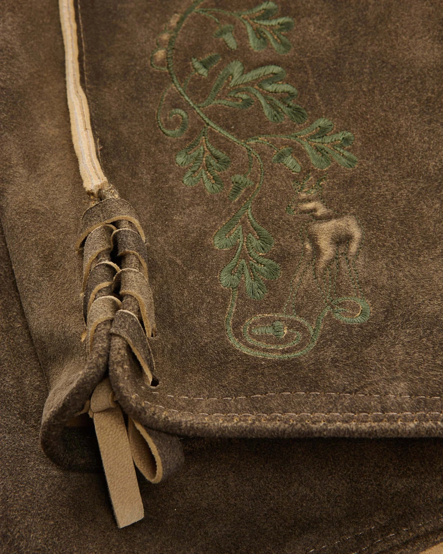 Brown leather bag with embroidered design of a nude figure and foliage.