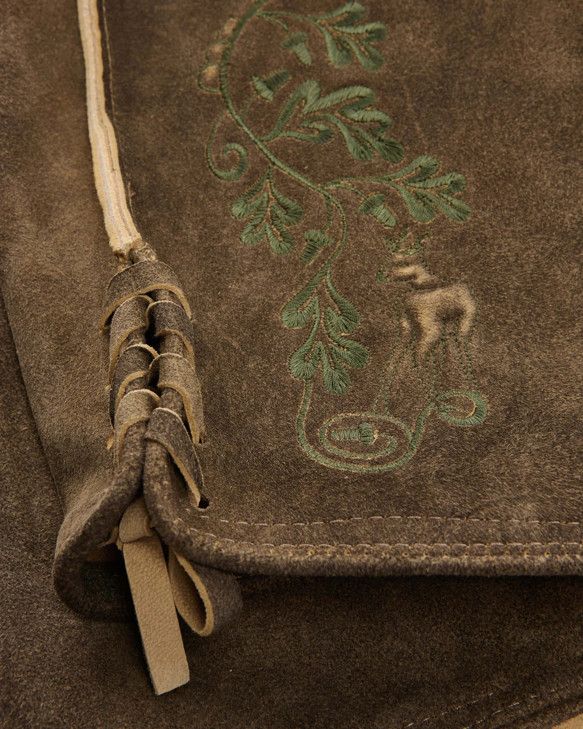 Brown leather bag with embroidered design of a nude figure and foliage.