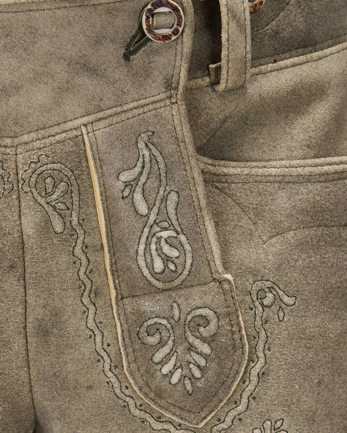 Close-up of a brown leather apron with intricate white embroidery on a matching background.