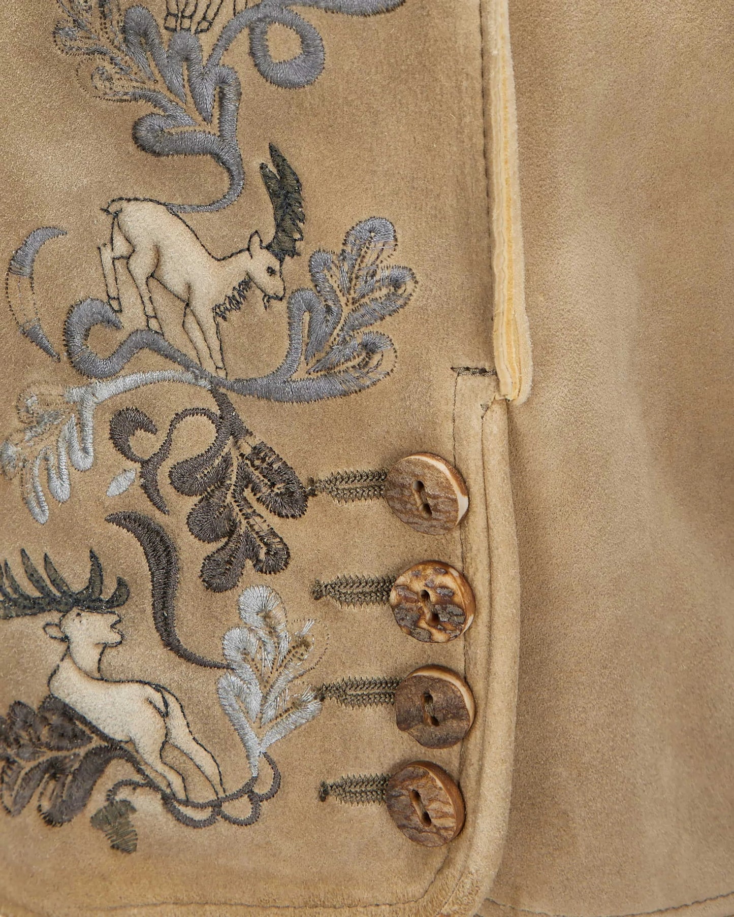 Close-up of a beige fabric with embroidered deer and floral patterns.