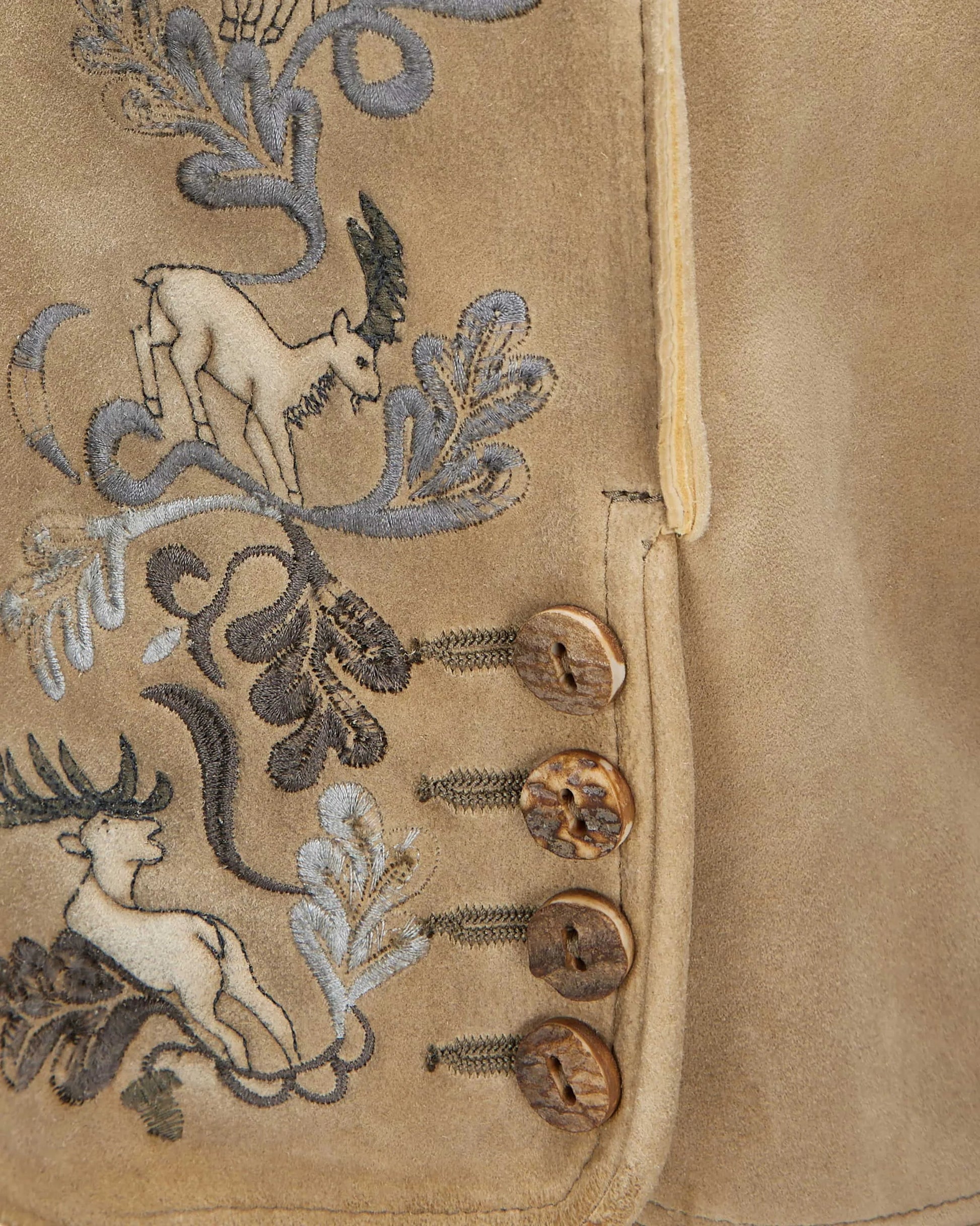 Close-up of a beige fabric with embroidered deer and floral patterns.