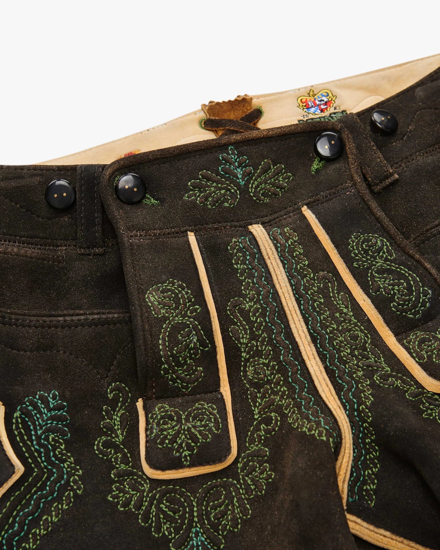 Close-up of a traditional black leather outfit with green embroidery on a white background