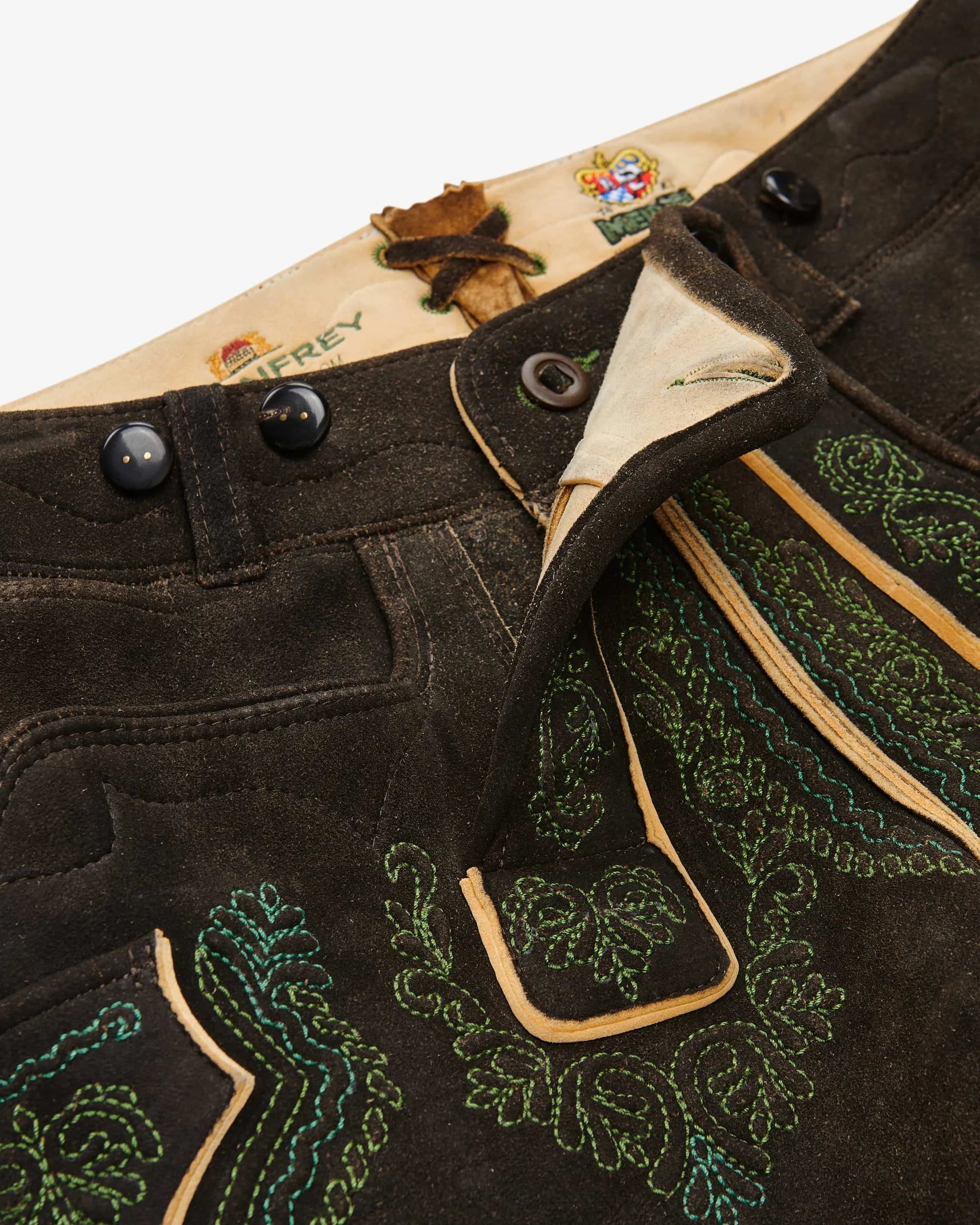 Close-up of a black leather jacket with green embroidery and buttons, featuring a brand logo on a white background.