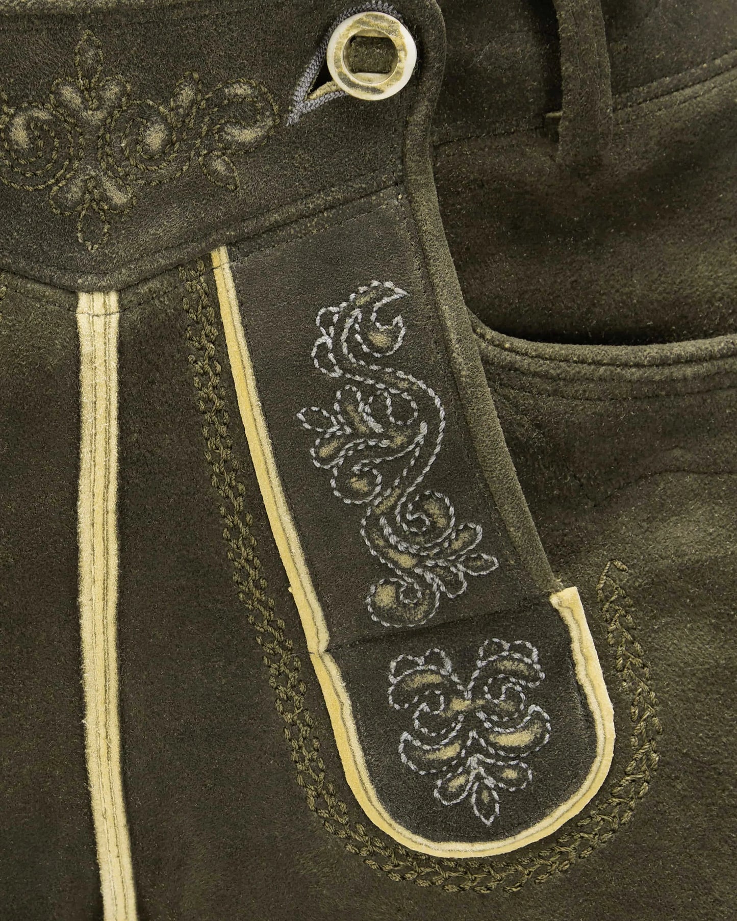 Close-up of dark brown leather with intricate white embroidery on a strap.