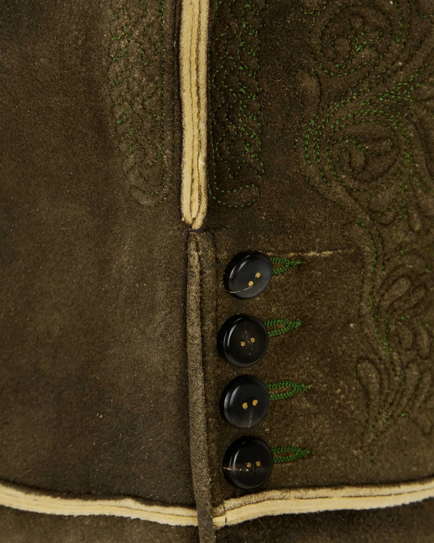 Close-up of a brown jacket with black buttons and intricate green embroidery.